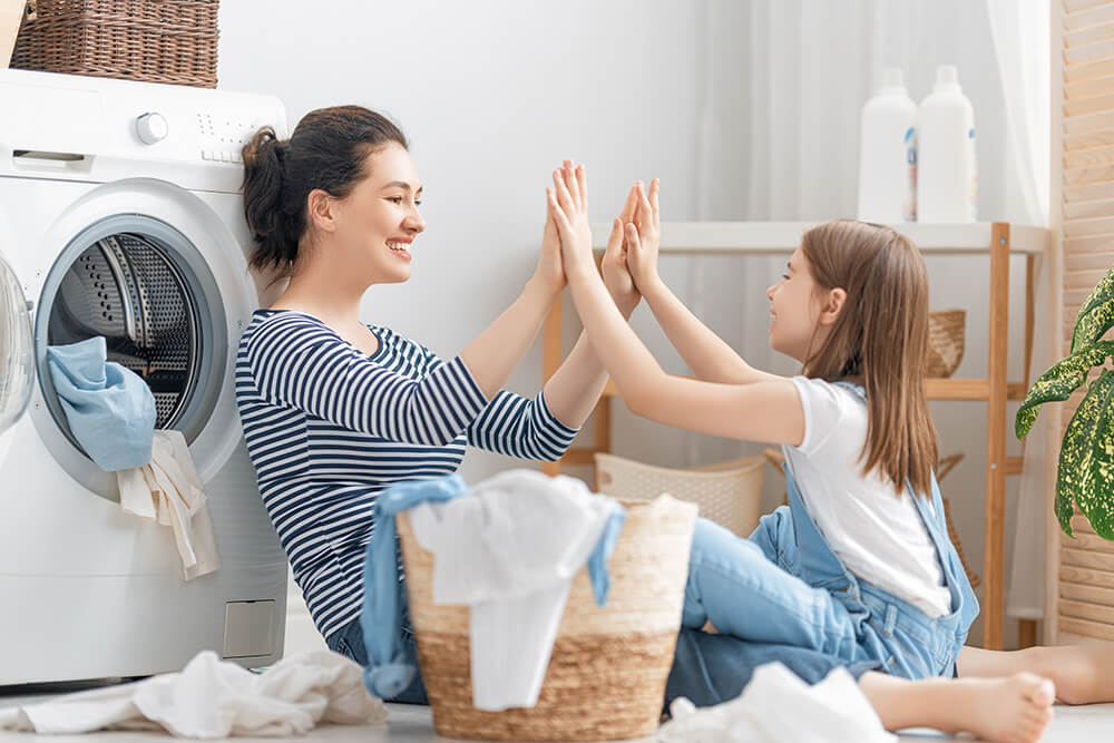 A woman and her young daughter having fun doing laundry together.