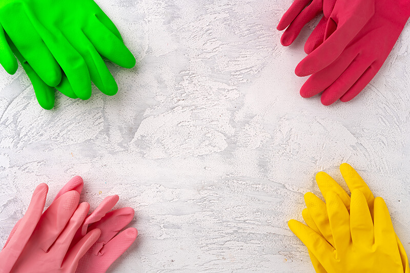 Four sets of rubber gloves in red, pink, yellow, and green laid out side by side.