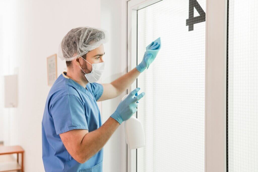Healthcare worker disinfecting a hospital room door.